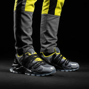 Gray and black sneakers with yellow accents worn by a person on a black background